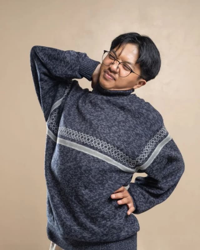 A man in a jumper holding his stiff neck and back