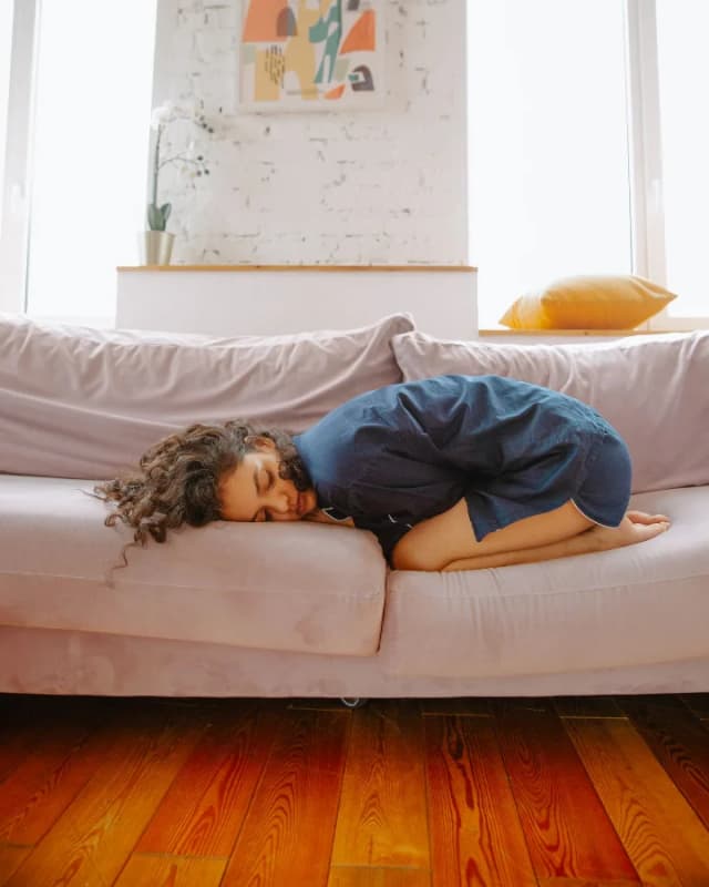 A woman curled up on a pink sofa with period pain