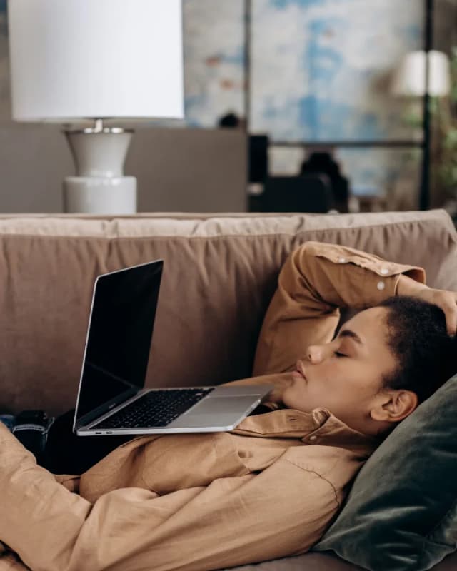 A woman lying on a sofa next to her laptop