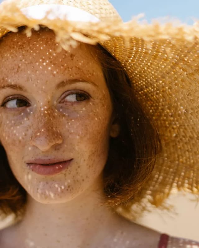A woman with freckles in a straw sun hat, outdoors