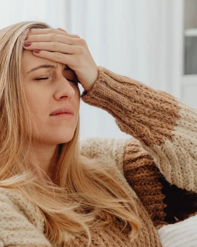 A woman in a knitted jumper holding her forehead, feeling dizzy