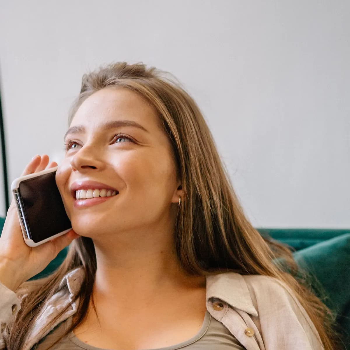 A smiling woman talks on her phone on a green sofa at home