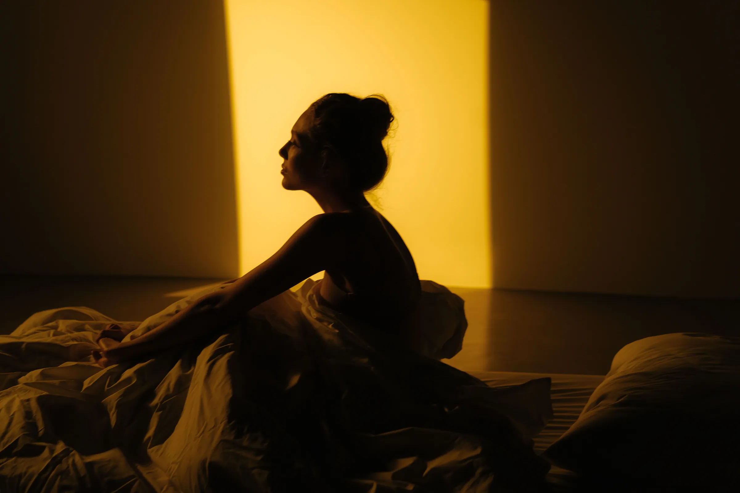 A woman sitting up in bed, silhouetted against warm evening light.