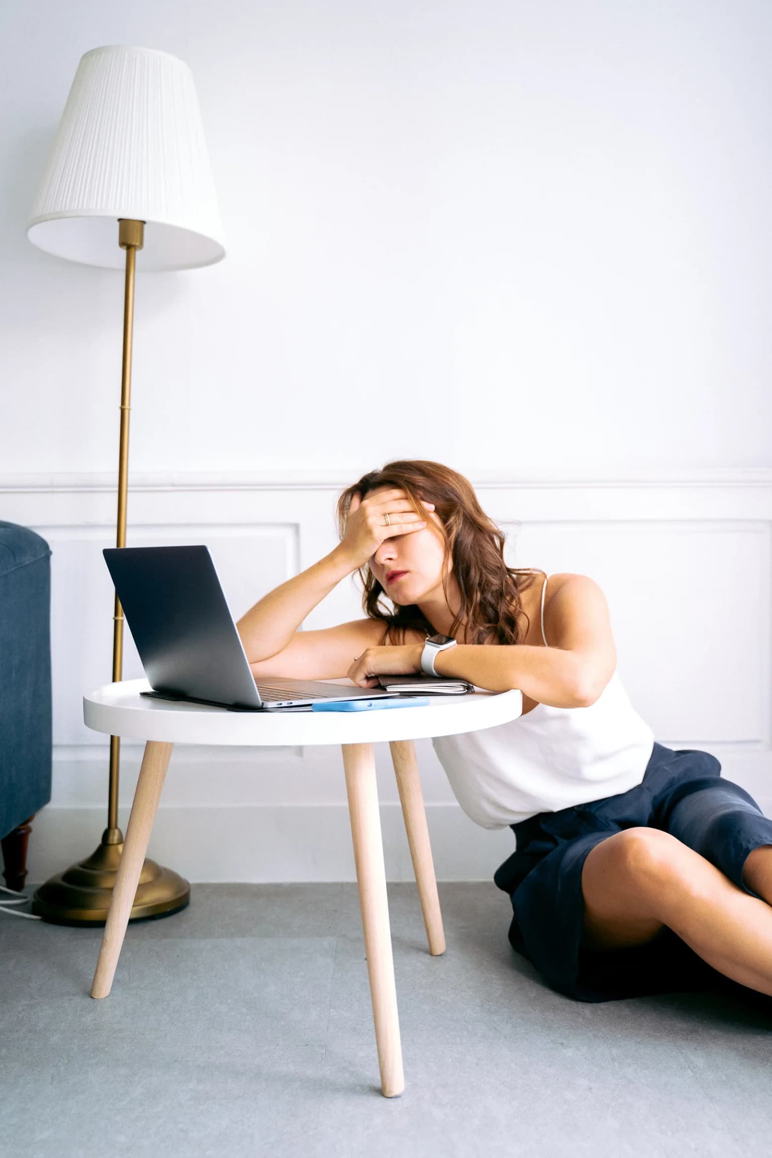 Person sitting beside a laptop with one hand resting on their forehead.