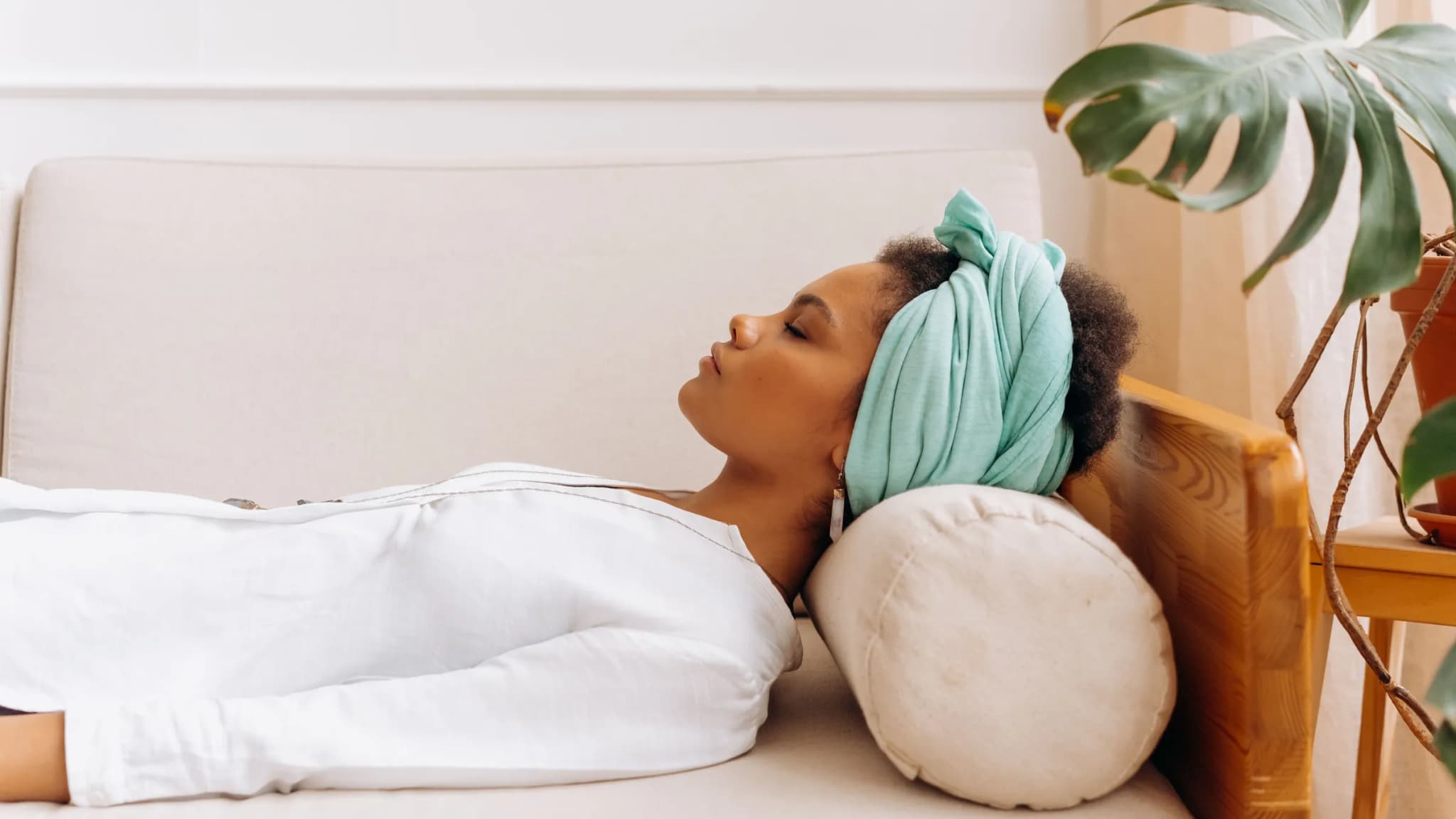 A woman in a headwrap lies on a sofa with her eyes closed, taking a rest