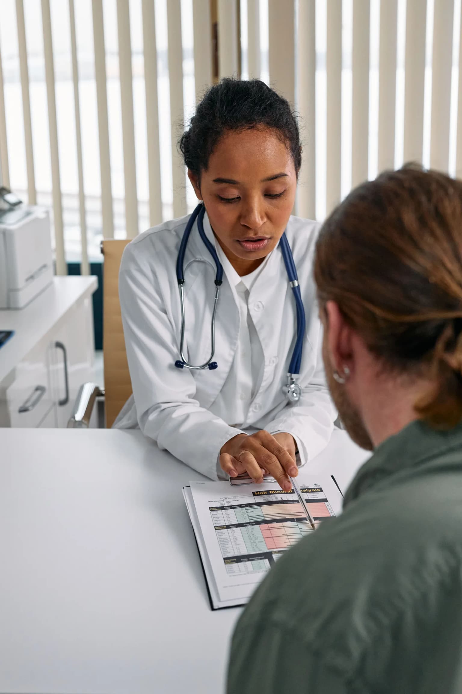 Doctor pointing to a printed chart while talking with a patient across a desk.