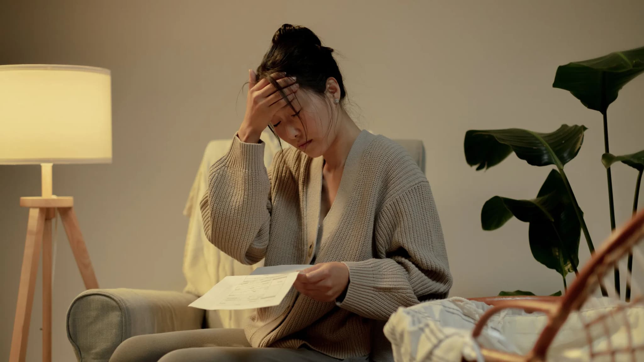 A woman at home holds her forehead while reading a printed sheet of paper