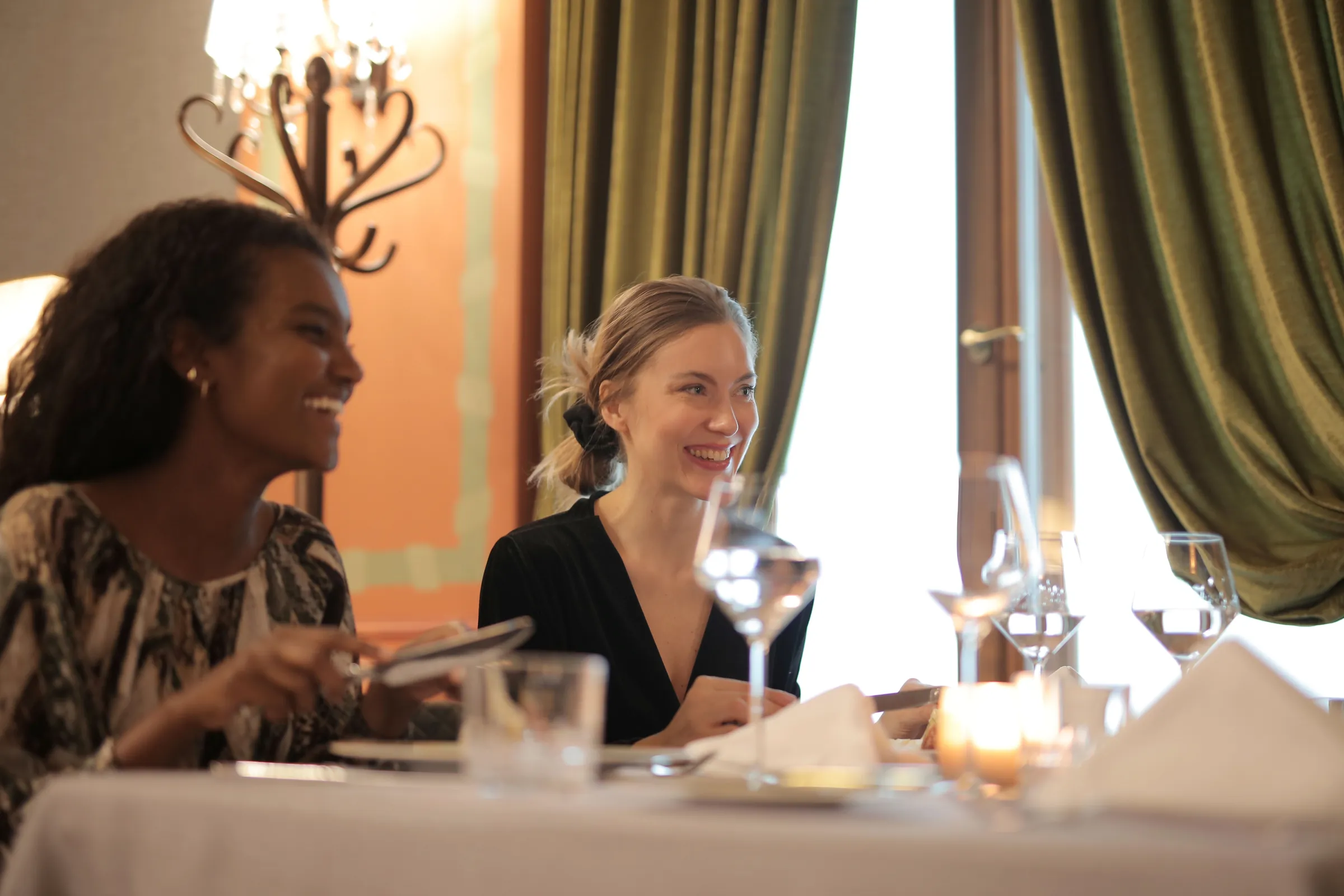 Two women laughing together at a restaurant table in warm light.