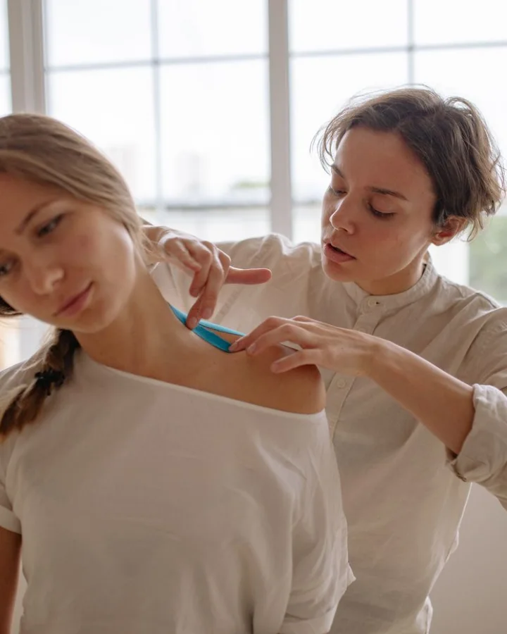 A woman having her shoulder taped by a physiotherapist