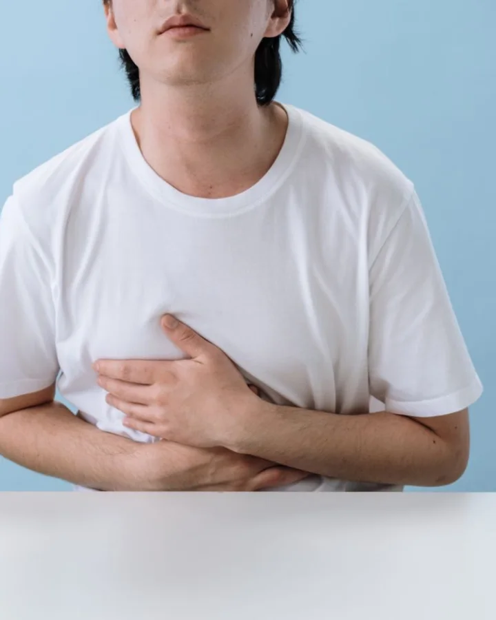 A young man in a white T-shirt holding his stomach