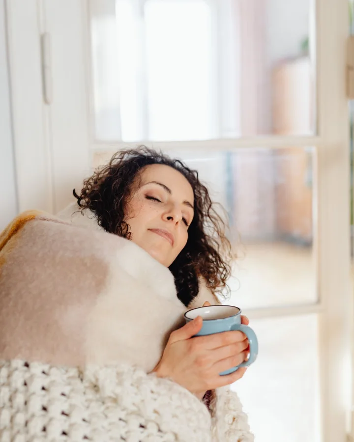 A woman wrapped in a blanket holding a warm mug