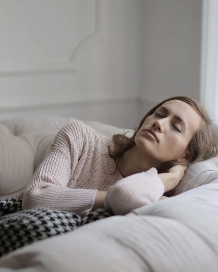 A woman lying on a sofa, resting with her eyes closed